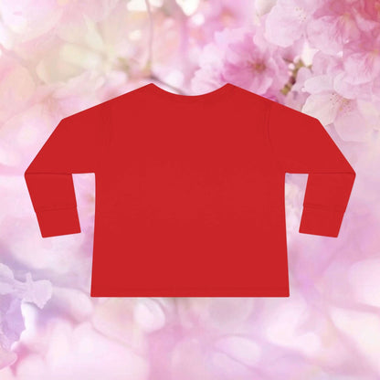 Back view of a vibrant red toddler flamingo long sleeve shirt on a floral background.