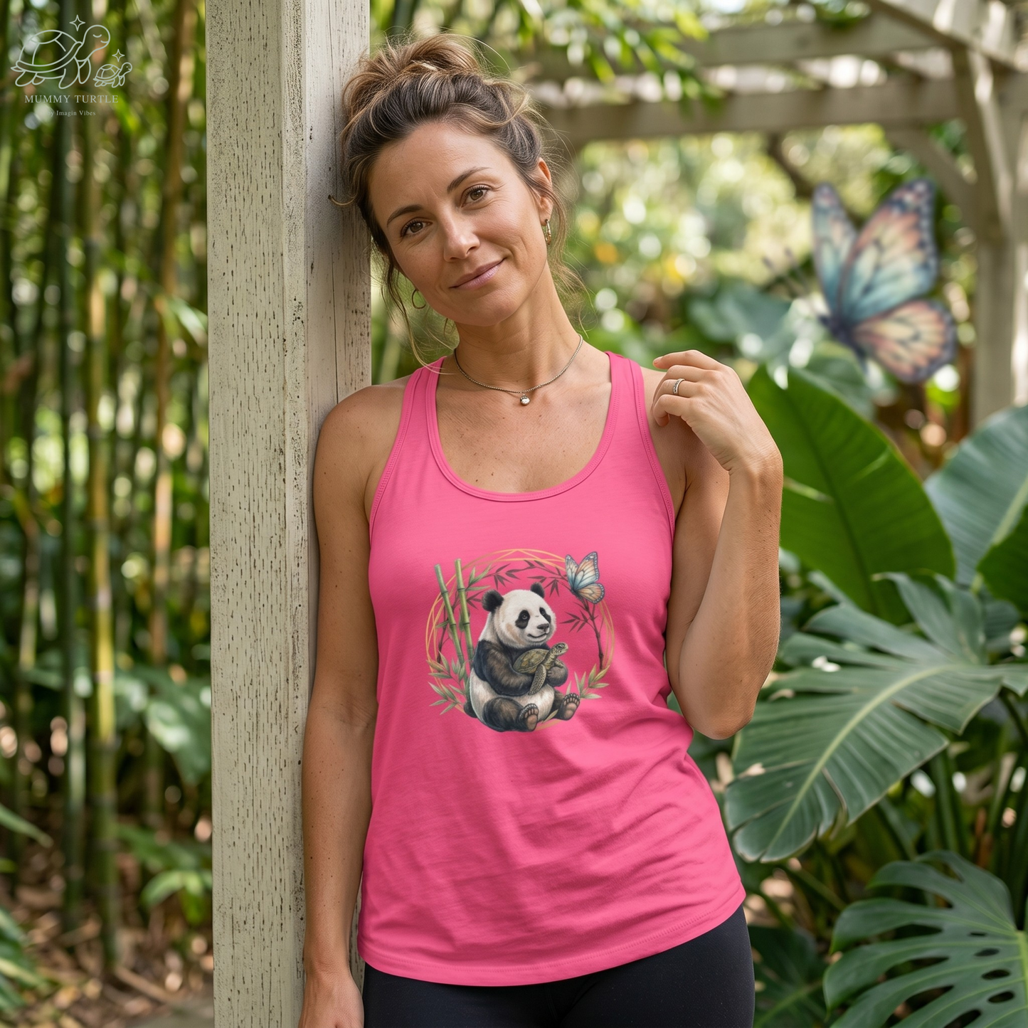 Woman wearing a pink Panda and turtle racerback tank beside bamboo with butterfly detail.