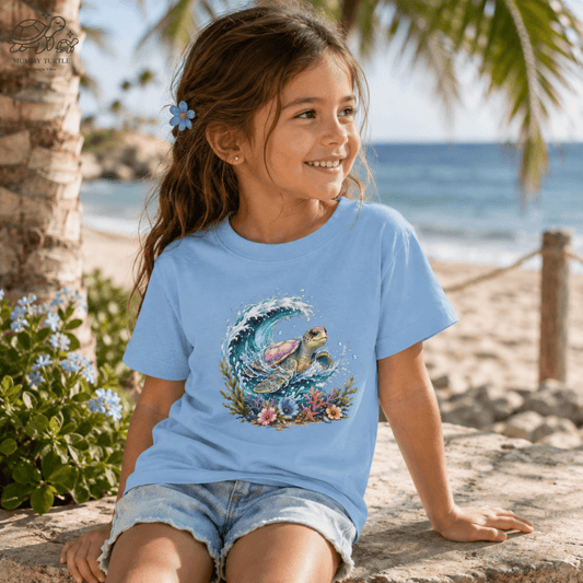 Child wearing the light blue Tidal Grace Kids Fine Jersey T-Shirt in a sunny coastal setting featuring the colorful sea turtle wave design.