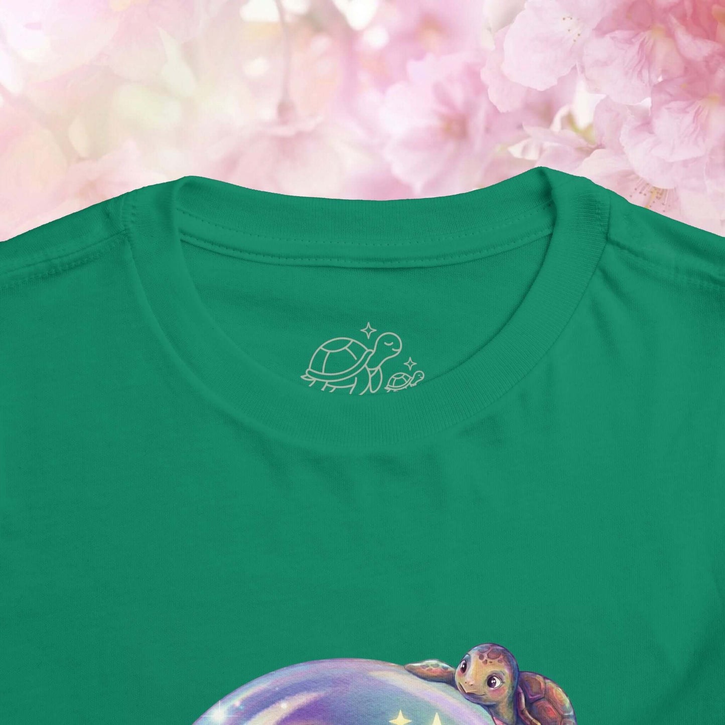 Close-up of the collar of a green toddler jellyfish t-shirt featuring a turtle design against a soft pink floral background.